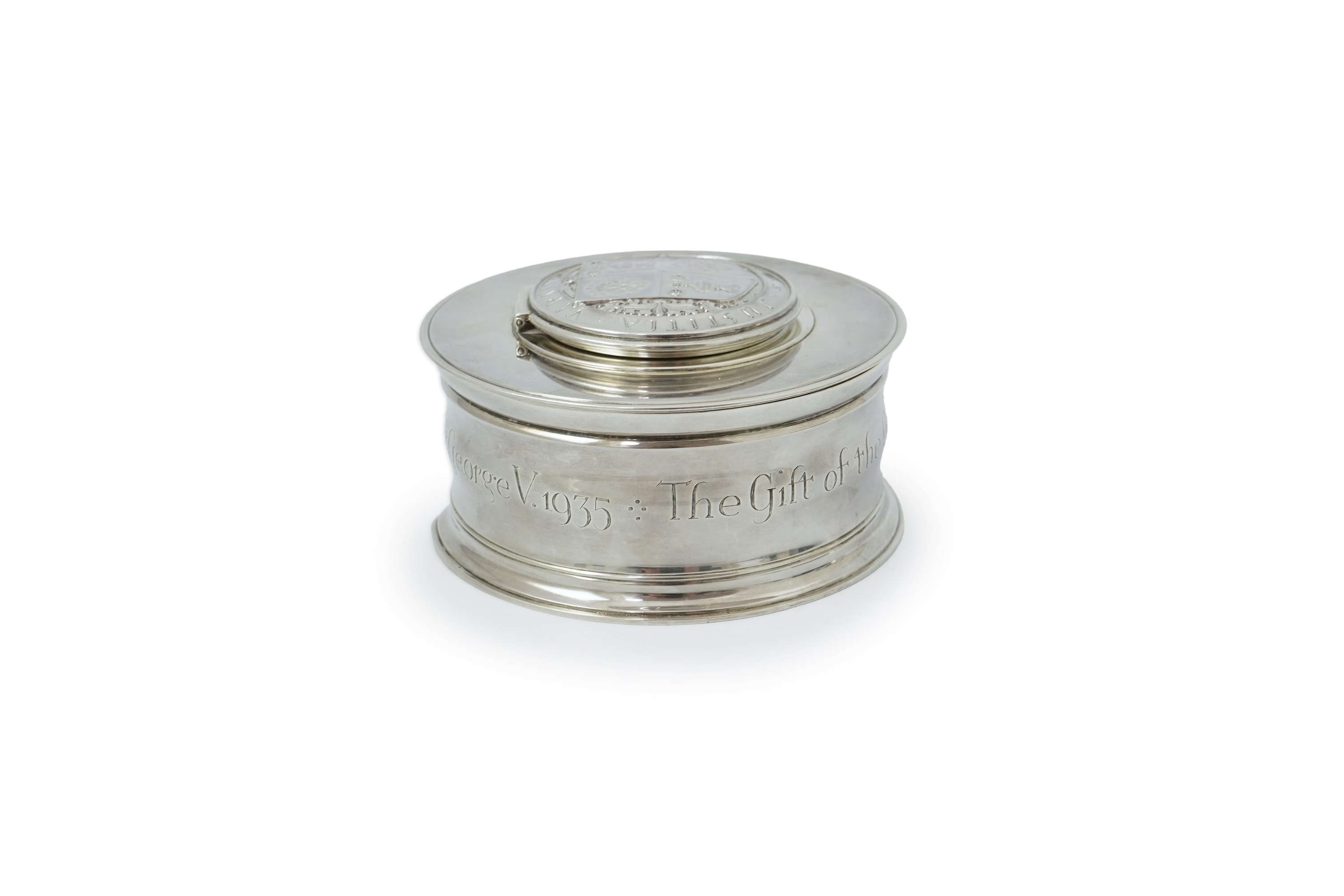 A George V silver circular inkwell, by Sebastian Garrard, commemorating the Silver Jubilee of King George V, the die stamped cover designed by George Kruger Gray featuring the Goldsmiths Company Coat of Arms